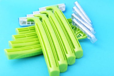 Mavi arka planda yeşil plastik tek kullanımlık tıraş bıçağı. Keskin kadın derisi jiletiyle tıraş olmak güvenli. Yüzünden ve bacaklarından kıllar alınmış. Bir kadının vücut bakımı ve güzelliği.