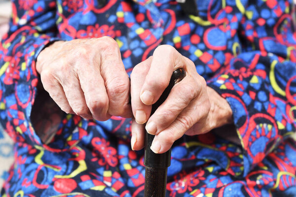 Пожилая женщина 90 лет положила руки на трость, пенсию и инвалидность, близко. Пожилые люди восприимчивы к вирусу, коронавирусу.