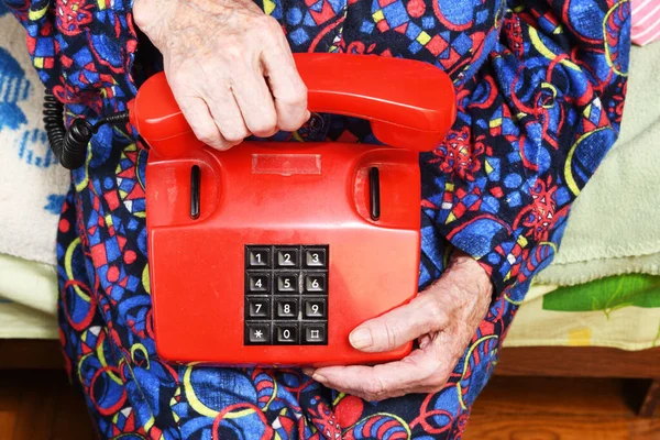 In her hands an old grandmother of 90 years holds in her hand a red old landline landline telephone, poverty and misery, hunger of the older generation.