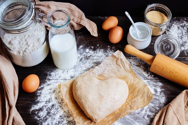 Cooking with love. Dough in heart shape top view. Baking ingredients on the wooden table — Stock Photo, Image