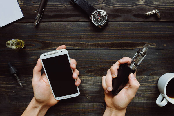 Man smoking vape or electronic cigarette and using smartphone. V