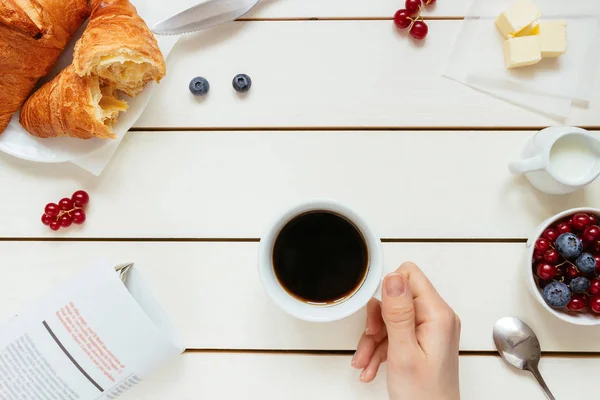 Tasty breakfast with coffee, berries, croissant on the white wooden table, top view