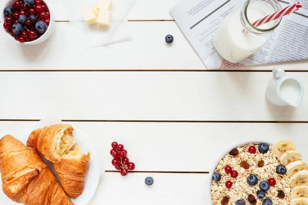 Desayuno saludable con copos de avena, bayas, croissants en la mesa de madera blanca con espacio para copiar, vista superior — Foto de Stock