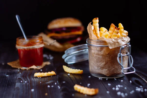 Smaczne frytki z sosem i burger na drewnianym stole czarny — Zdjęcie stockowe