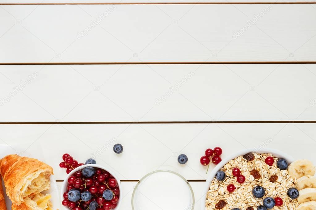 Healthy breakfast with berries, croissant and milk on the white wooden table with copy space, top view