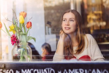 Kafede oturan ve düşünceli pencereden dışarı bakıyor güzel gülümseyen genç kadın