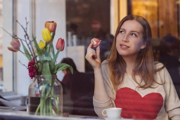 Hermosa joven soñadora sentada en una cafetería cerca de la ventana, tomando café y comiendo postre —  Fotos de Stock