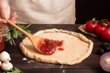 Pizza yemek. Taze domates sosu pizza hamuru için ekleme eller. Pizza malzemeleri ahşap tablo