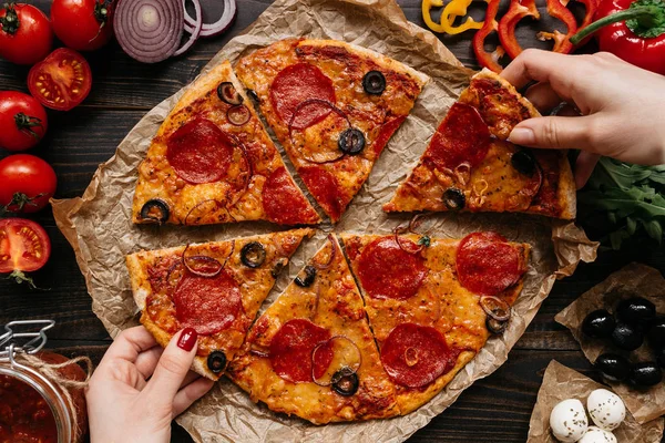Comer pizza, vista superior. Las manos tomando rebanadas de pizza delirante caliente. Ingredientes de pizza en la mesa de madera — Foto de Stock