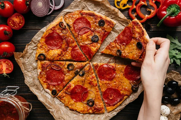 Comer pizza, vista superior. Mano tomando rebanada de pizza delirante caliente. Ingredientes de pizza en la mesa de madera — Foto de Stock