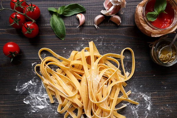 Fresh homemade pasta and vegetables on the dark wooden table top view