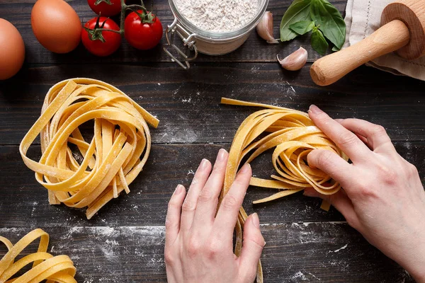 Female hands making fresh homemade pasta. Pasta ingredients on the dark wooden table top view