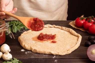 Pizza yemek. Taze domates sosu pizza hamuru için ekleme eller. Pizza malzemeleri ahşap tablo