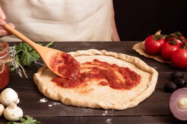 Pizza yemek. Taze domates sosu pizza hamuru için ekleme eller. Pizza malzemeleri ahşap tablo