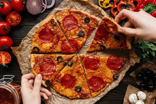 Comer pizza, vista superior. Las manos tomando rebanadas de pizza caliente deliciosa. Ingredientes de pizza en la mesa de madera — Foto de Stock