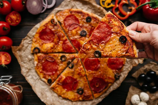 Comer pizza, vista superior. Mano tomando rebanada de pizza caliente deliciosa, enfoque selectivo. Ingredientes de pizza en la mesa de madera — Foto de Stock
