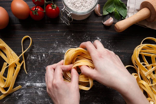 Female hands making fresh homemade pasta. Pasta ingredients on the dark wooden table top view