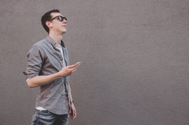 Onun smartphone kullanarak, müzik dinleme genç hipster adam. Gri arka planı