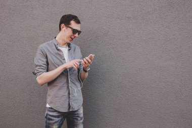 Onun smartphone kullanarak, müzik dinleme genç hipster adam. Gri arka planı