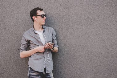 Onun smartphone kullanarak, müzik dinleme genç hipster adam. Gri arka plan, kopya alanı