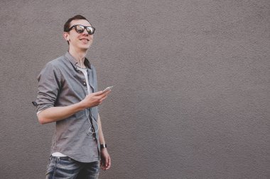 Onun smartphone kullanarak, müzik dinleme genç hipster adam. Gri arka planı