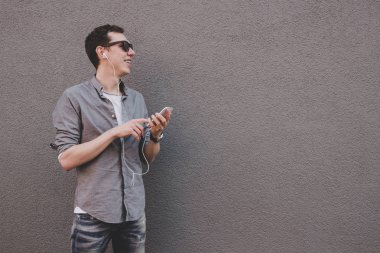 Onun smartphone kullanarak, müzik dinleme genç hipster adam. Gri arka planı