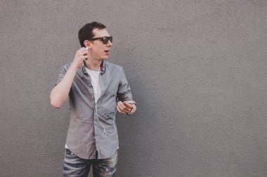 Onun smartphone, müzik dinleme kullanan genç gülmek hipster adam. Gri arka plan, kopya alanı