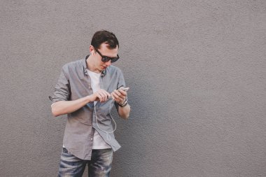 Onun smartphone, müzik dinleme kullanan genç gülmek hipster adam. Gri arka plan, kopya alanı