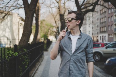 Yürüyen genç adam, vaping elektronik sigara veya vape. Kopya alanı ile