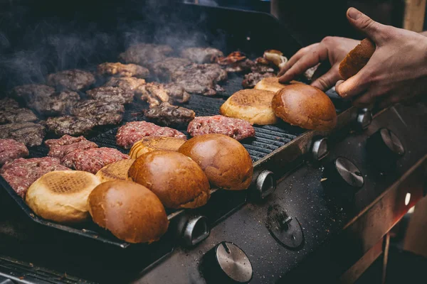 Cozinhar deliciosos hambúrgueres de carne suculentos e pães na grelha — Fotografia de Stock