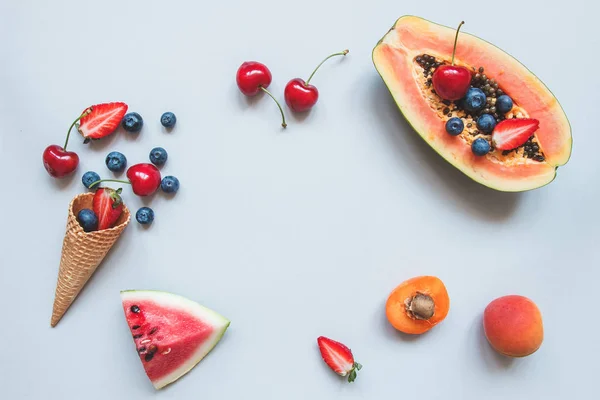 Fondo de verano. Bayas jugosas frescas, papaya y cono de waffle dulce en el fondo azul — Foto de Stock