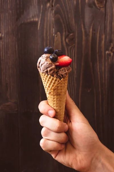 Hands holding chocolate ice-cream with berries on the wooden background — Stock Photo, Image