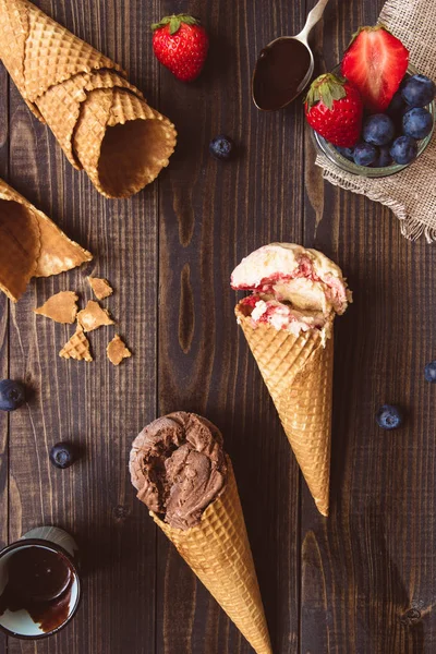 stock image Ice-cream with fresh berries and chocolate sauce on the wooden background, top view