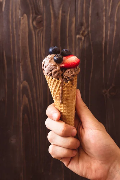 Hands holding chocolate ice-cream with berries on the wooden background — Stock Photo, Image