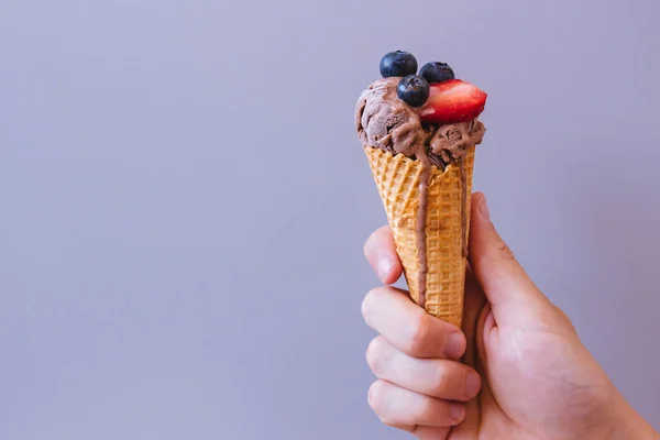 Hands holding chocolate ice-cream with blueberry and strawberry, with copy space — Stock Photo, Image