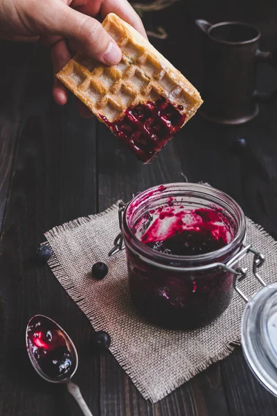 Gofre belga de mano con mermelada en la mesa de madera oscura. Comer delicioso postre — Foto de Stock