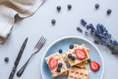 Yaban mersini ve hafif mavi masa üzerinde çilek ile ev yapımı Belçika waffle