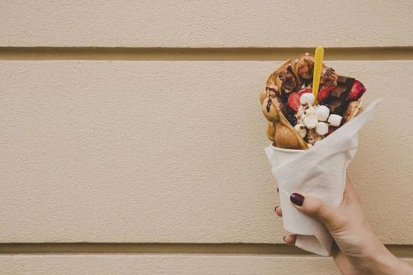 Hand holding bubble waffle with fruits, chocolate and marshmallow, with copy space — Stock Photo, Image