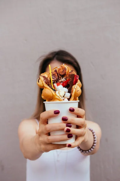 Young woman holding bubble waffle with fruits, chocolate and marshmallow, selective focus — Stock Photo, Image