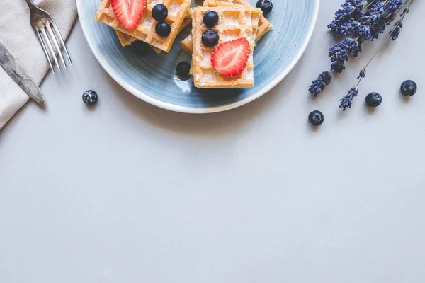 Zelfgemaakte Belgische wafels met bosbessen en aardbeien op de blauwe lichttafel met kopie ruimte — Stockfoto