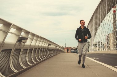 Şehrin modern köprü üzerinde çalışan, smartphone cep telefonu ile müzik dinleme genç adam