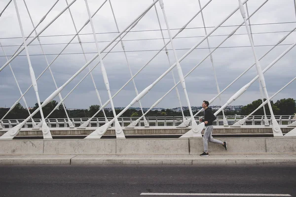 Şehrin modern köprü üzerinde çalışan, smartphone cep telefonu ile müzik dinleme genç adam