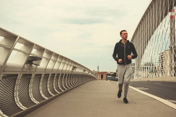 Şehrin modern köprü üzerinde çalışan, smartphone cep telefonu ile müzik dinleme genç adam