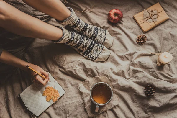 Confortable maison. Femme avec une tasse de boisson chaude écrit dans un bloc-notes. Vue du dessus — Photo