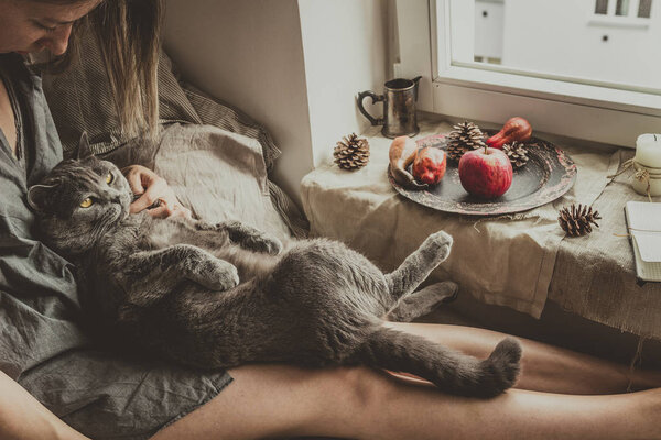 Cozy home. Woman with cute cat sitting in bed by the window — Stock Photo, Image