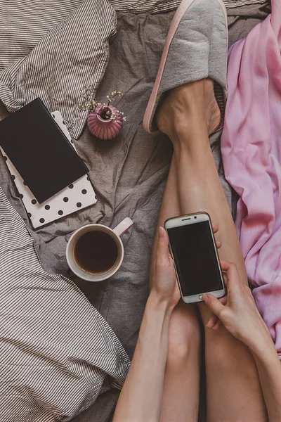 Kadın yatakta evde oturan ve smartphone, üstten görünüm kullanma