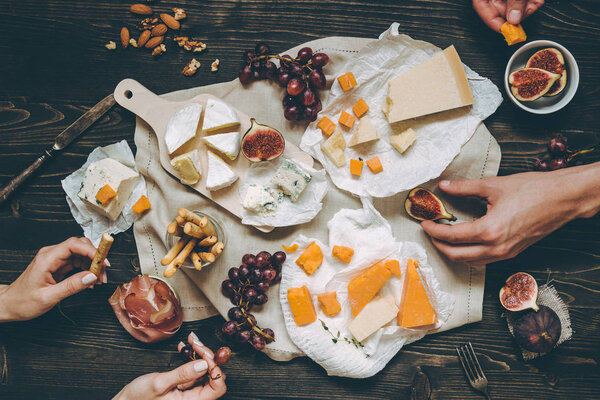 Eating various types of cheese with fruits and snacks on the wooden dark table.