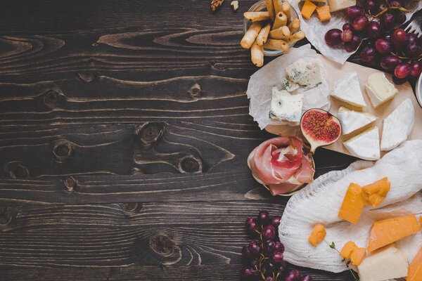 Various types of cheese with fruits and snacks on the wooden dark table with copy space