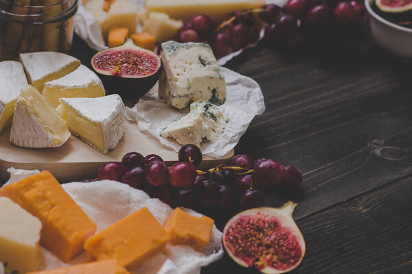 Various types of cheese with fruits on the wooden dark table. Selective focus