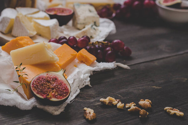 Various types of cheese with fruits and nuts on the wooden dark table. Selective focus